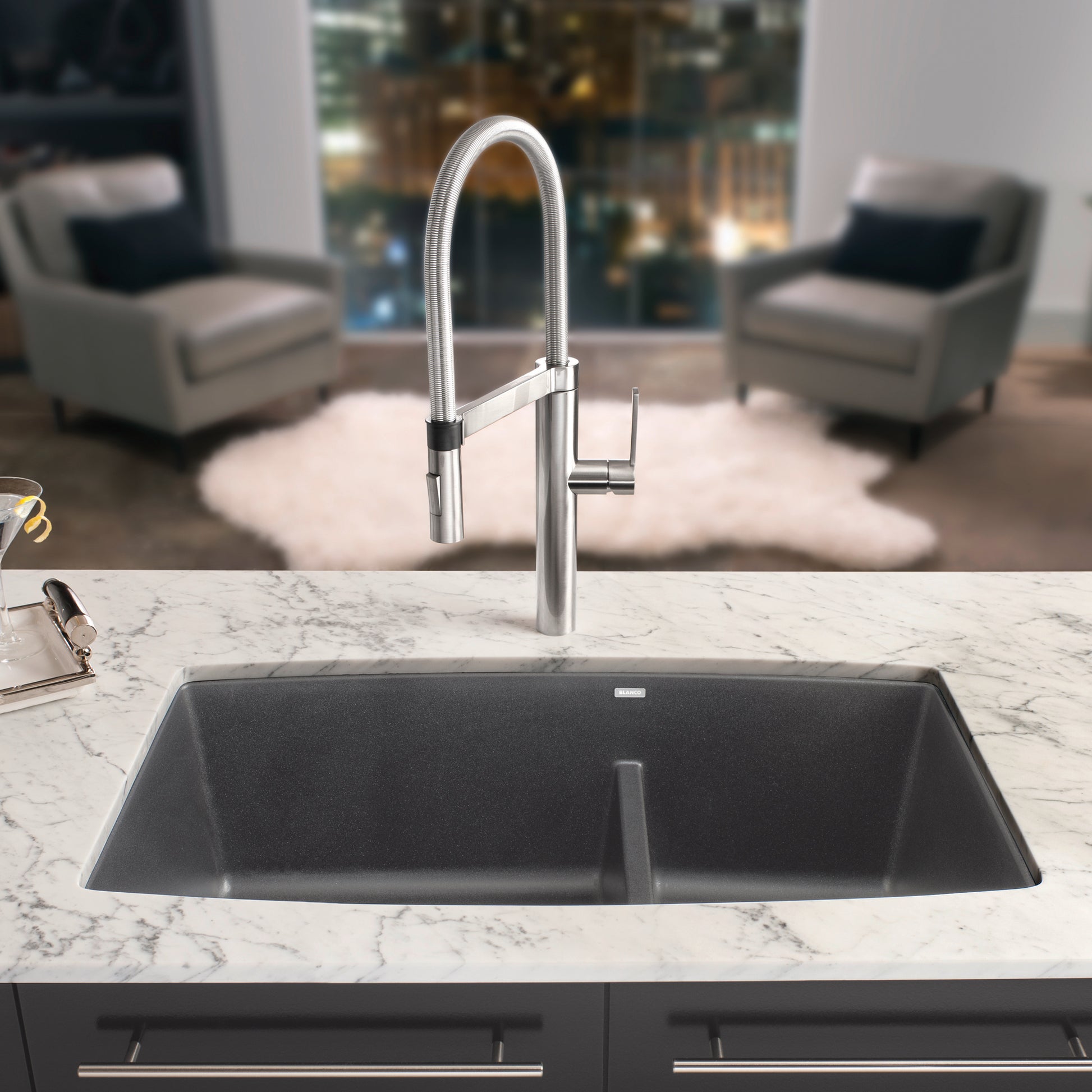 Cinder gray undermount sink with two bowls and stainless steel pull-down faucet installed in marble countertop.