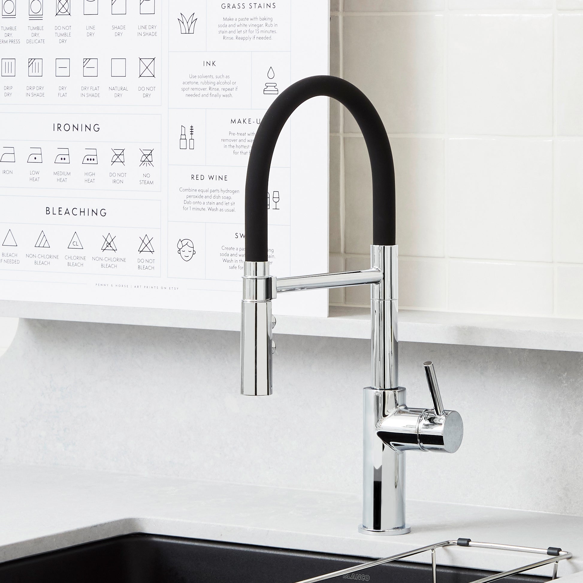 Chrome kitchen faucet with black flexible hose and single lever handle mounted on white countertop.