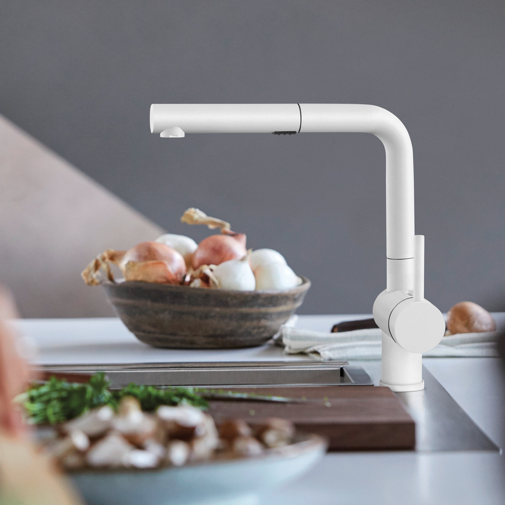 White pull-out kitchen faucet with angled spout and rotatable handle mounted on countertop sink.