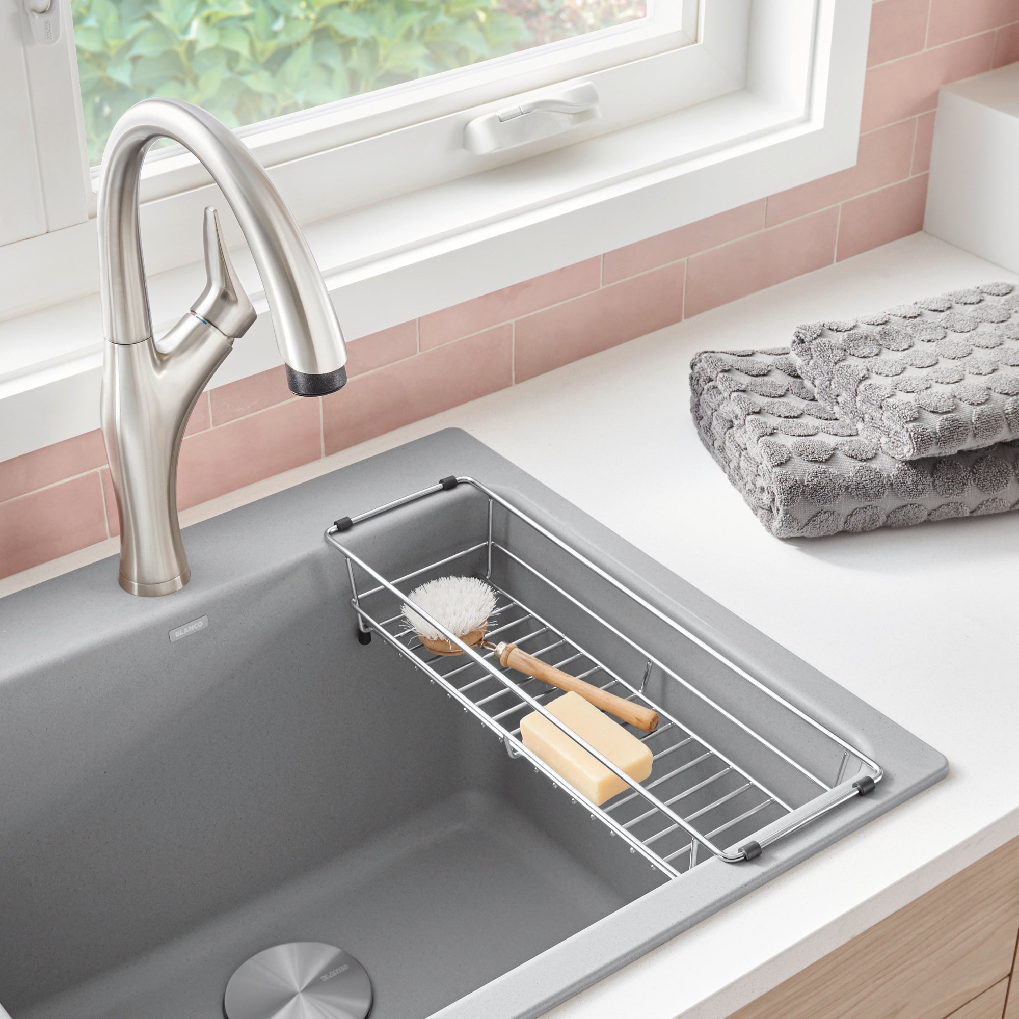 Stainless steel basket with dividers positioned inside a gray laundry sink, holding cleaning brushes and supplies.