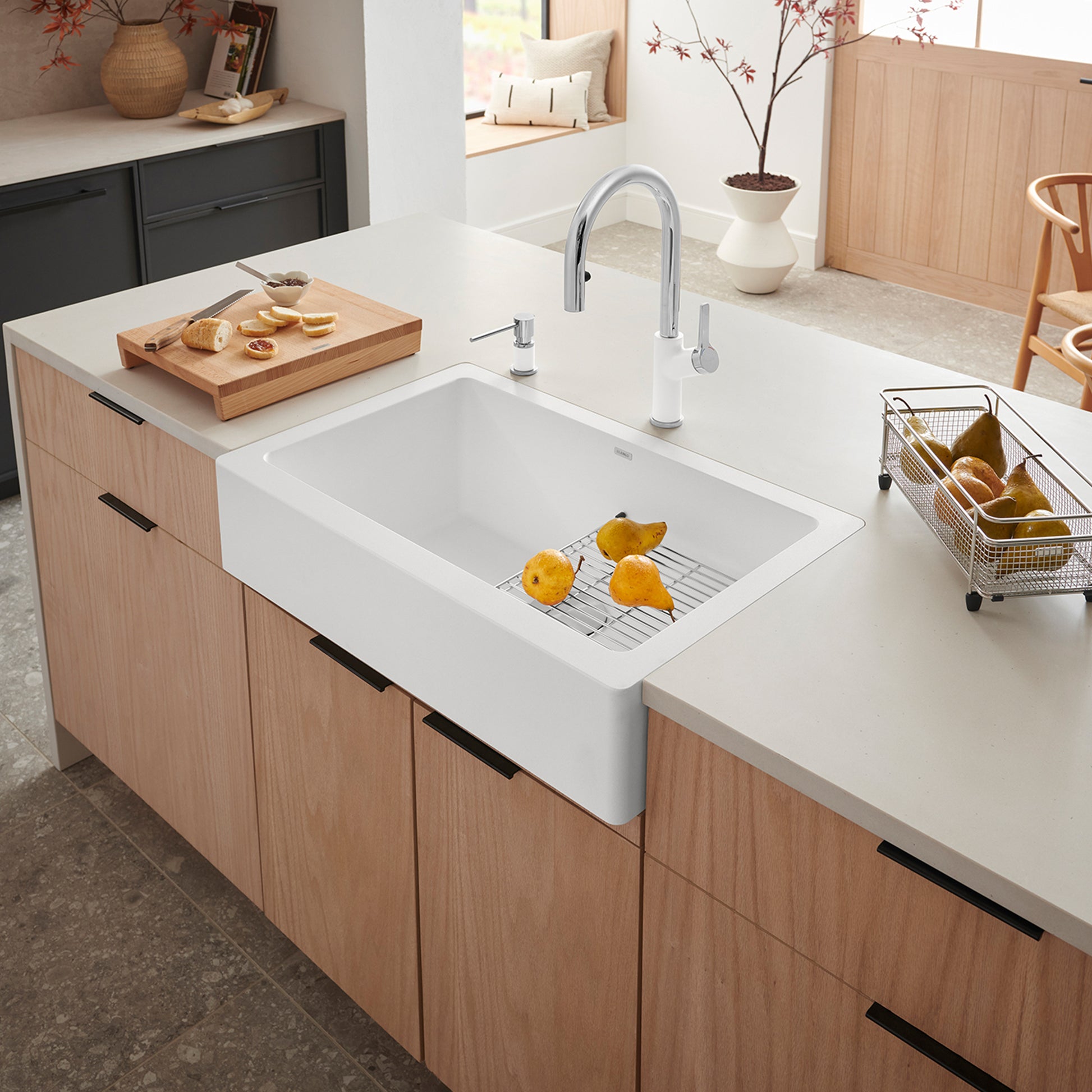 White farmhouse sink with single basin, grill rack, and pull-down faucet installed in light wood cabinetry.