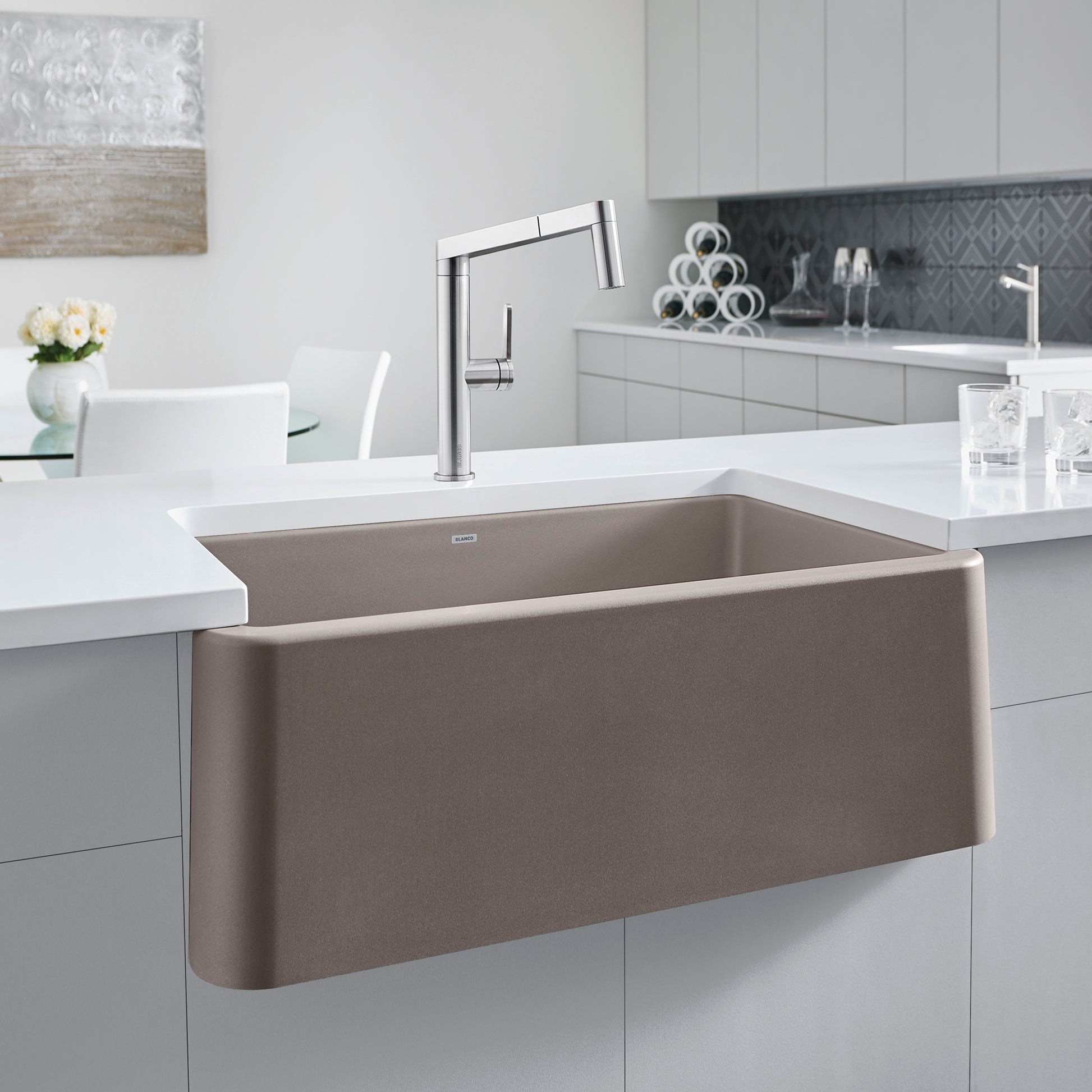 Truffle-colored single bowl farmhouse sink with curved apron front, installed in white kitchen counter with chrome faucet.