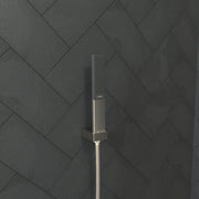 Brushed nickel rectangular handheld showerhead with perforated spray face mounted on a vertical hose against herringbone tile