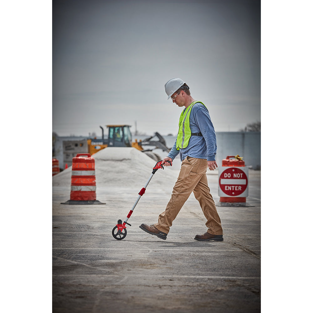 Worker using a red and black measuring wheel on a concrete surface at a construction site.