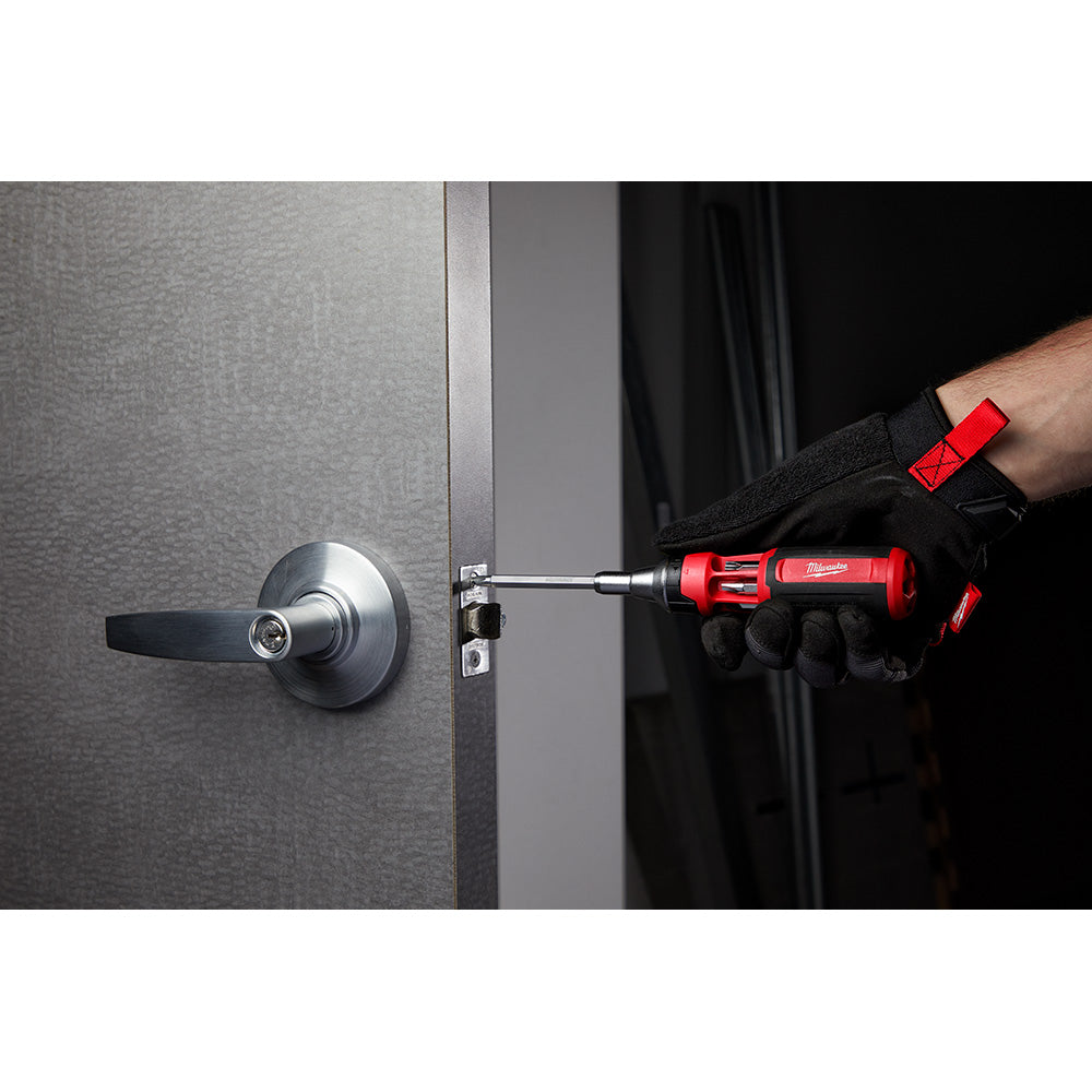 Red and black Milwaukee ratcheting multi-bit driver being used to install a lock on a door.