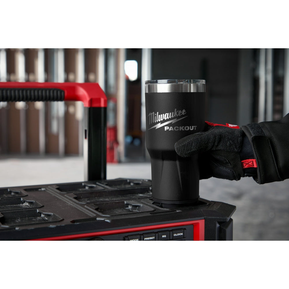 Black insulated tumbler with stainless steel rim and Milwaukee PACKOUT logo, displayed on toolbox.