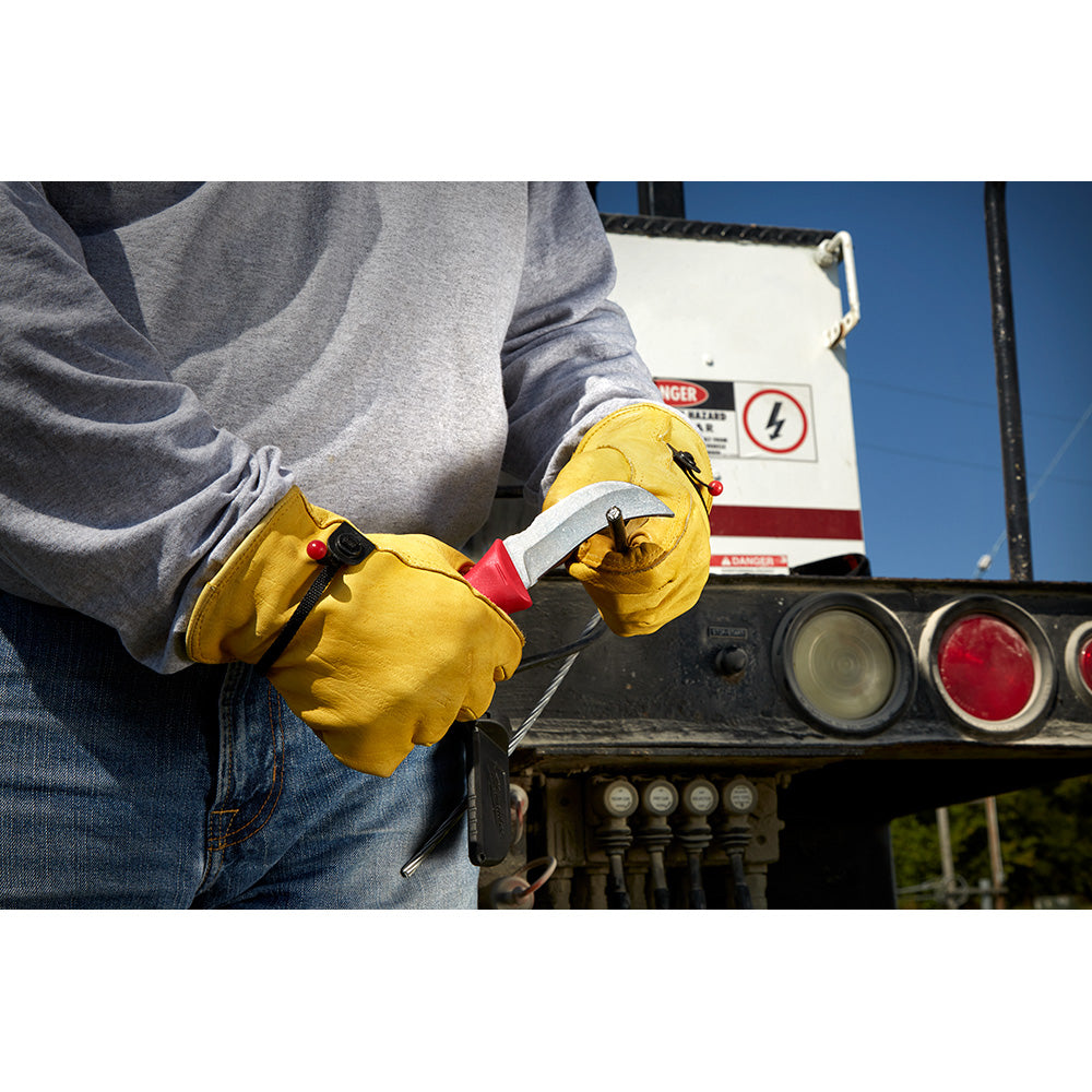 Person wearing yellow work gloves holding a fixed blade knife with curved hawkbill blade and red handle detail.