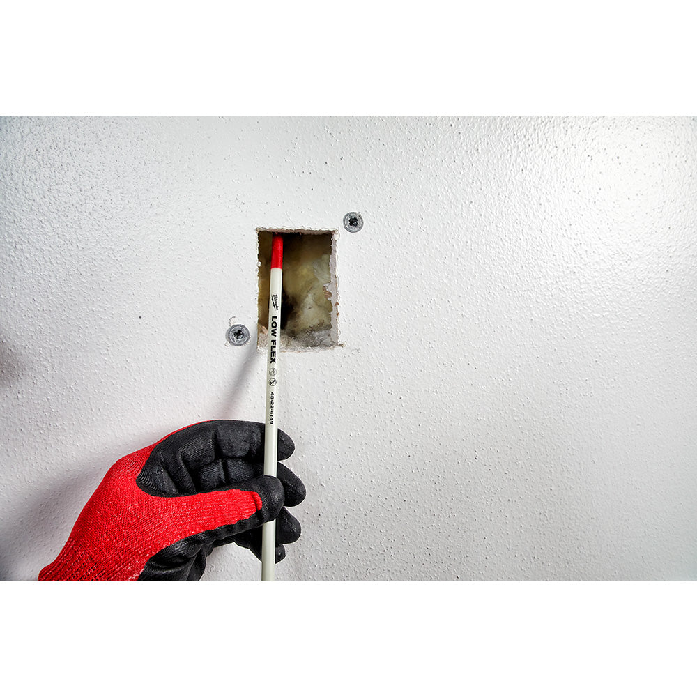 Hand in red and black glove inserting white fish stick through wall opening to route wire through conduit.