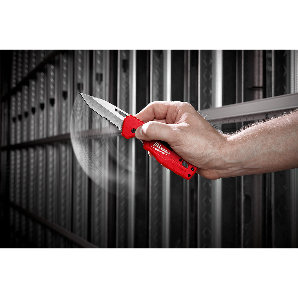 Hand holding open red Milwaukee folding knife with serrated blade against industrial metal background.
