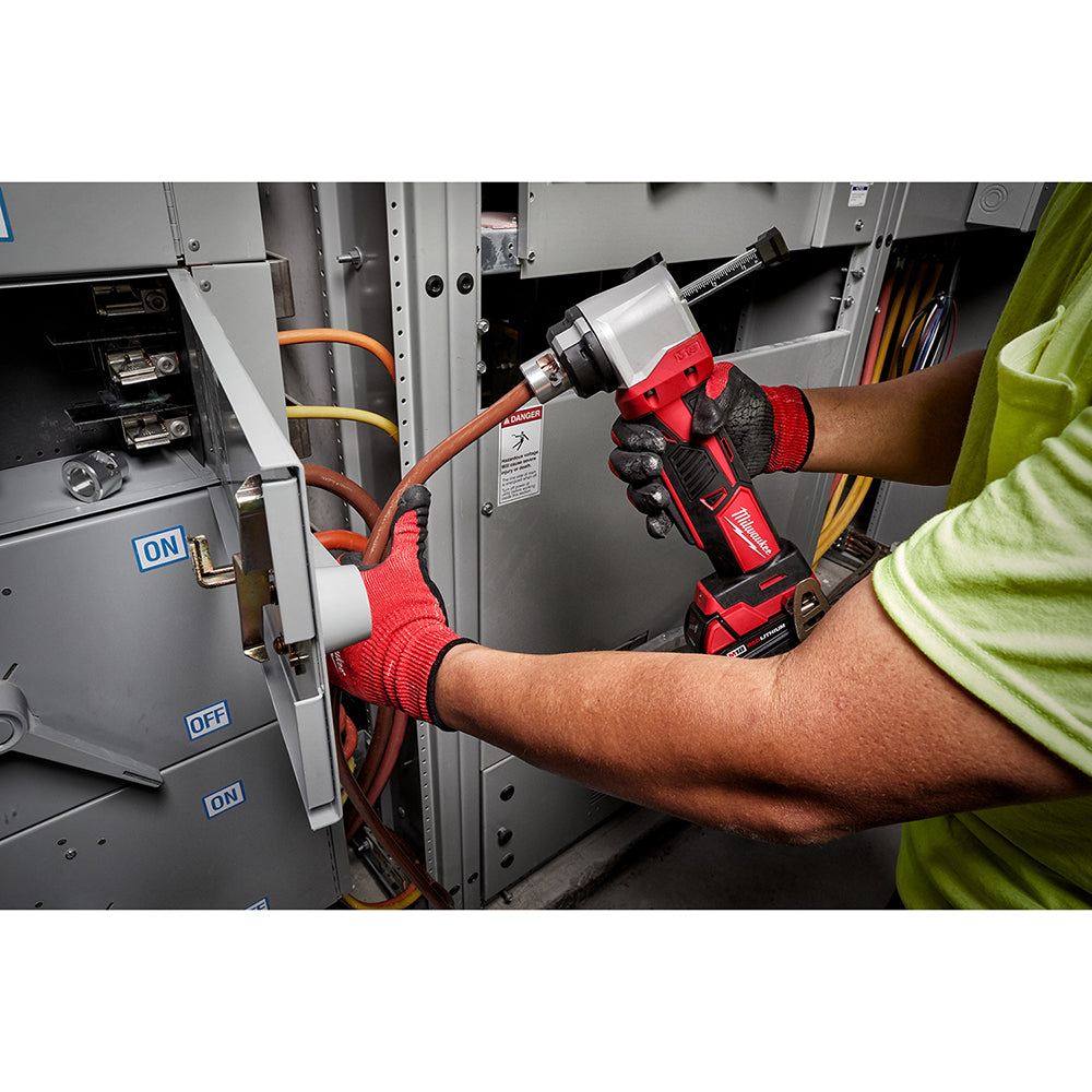 Red and black cordless cable stripper being used on orange electrical wire by a worker wearing gloves.
