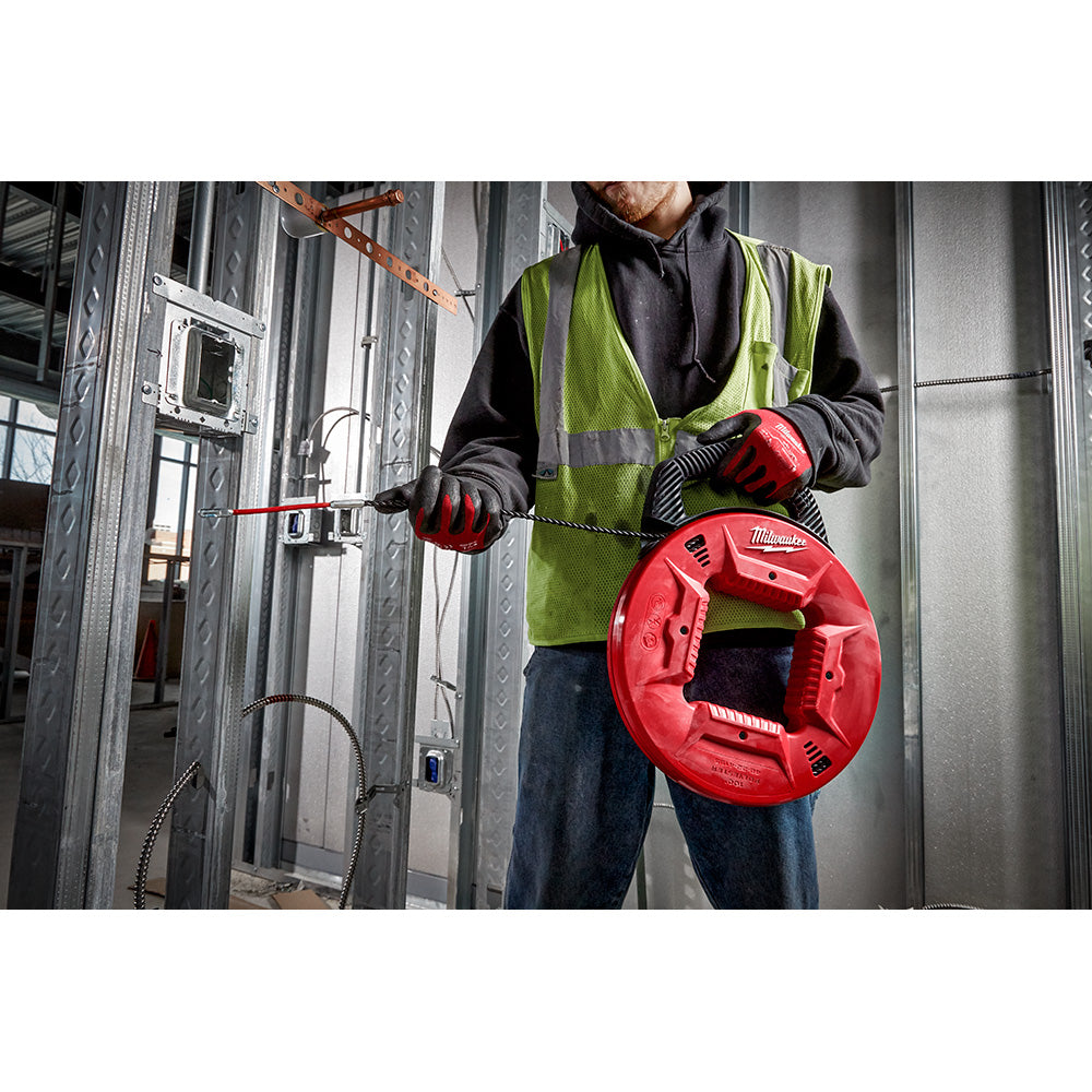 Red Milwaukee fish tape reel with flexible metal leader being held by a worker in a safety vest during electrical conduit ins