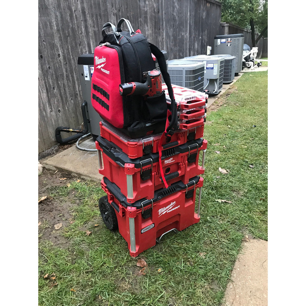 Red and black Milwaukee PACKOUT backpack worn on top of stacked red storage containers with wheels.