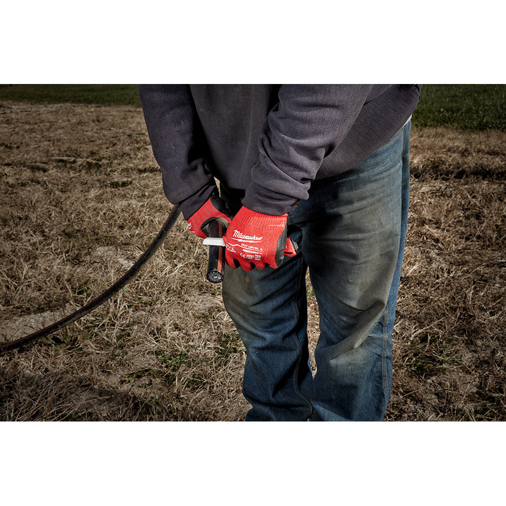 Person wearing red Milwaukee work gloves holding a black lineman underground knife with cable in outdoor setting.