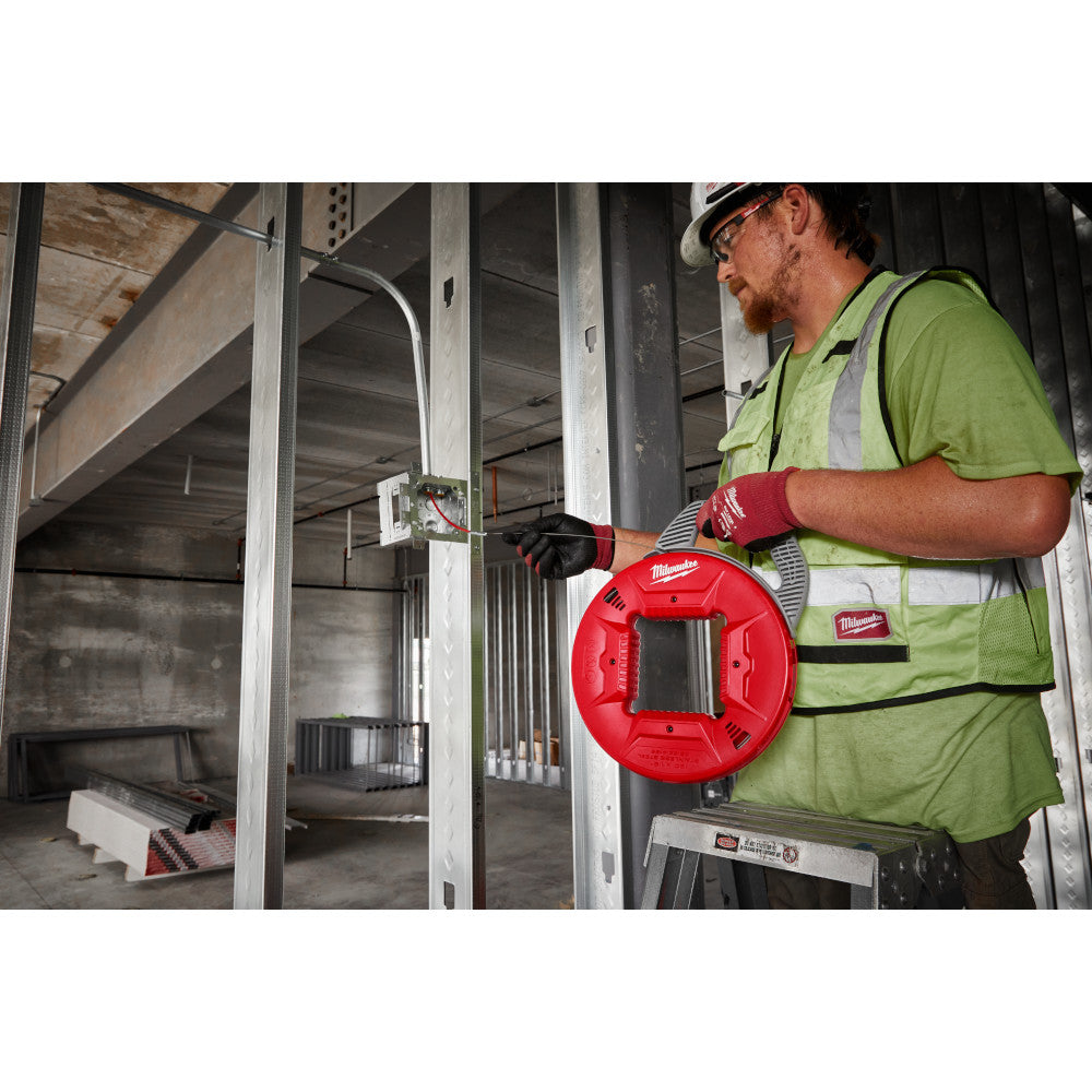 Worker in safety gear holding red Milwaukee fish tape reel with metal guide hook during electrical installation.