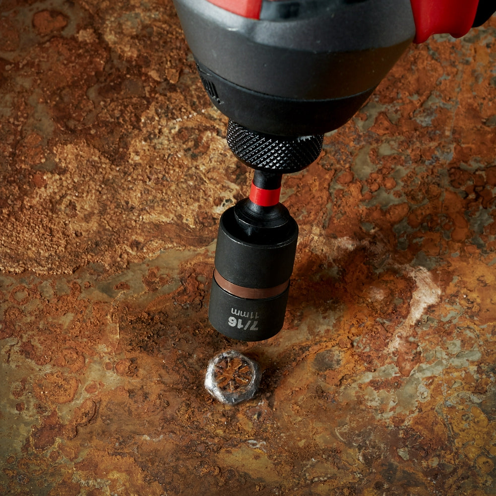 Black and red impact extractor bit being used to remove a stuck screw from a rusted metal surface.