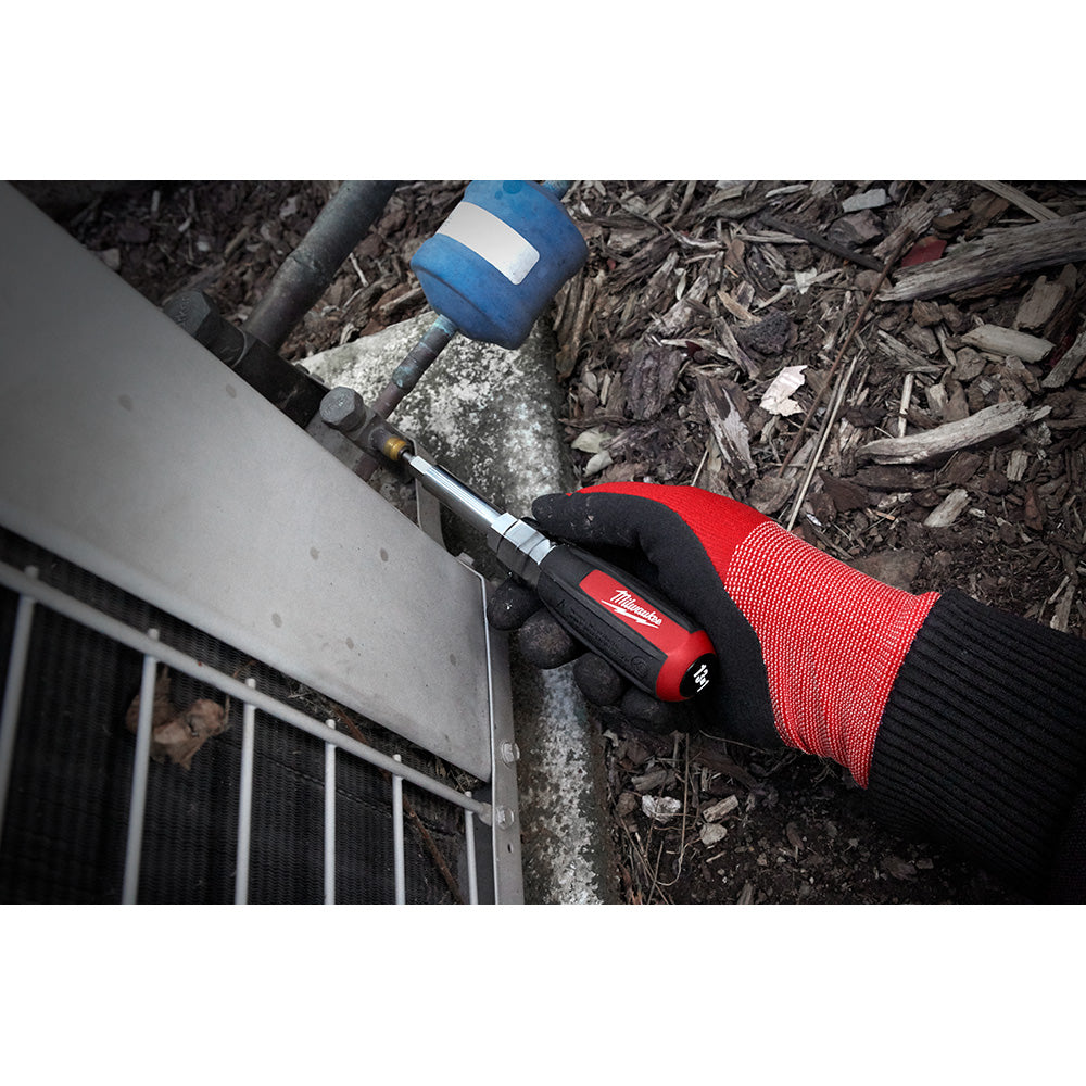 Milwaukee screwdriver with red and black cushion grip handle held in gloved hand on outdoor surface.