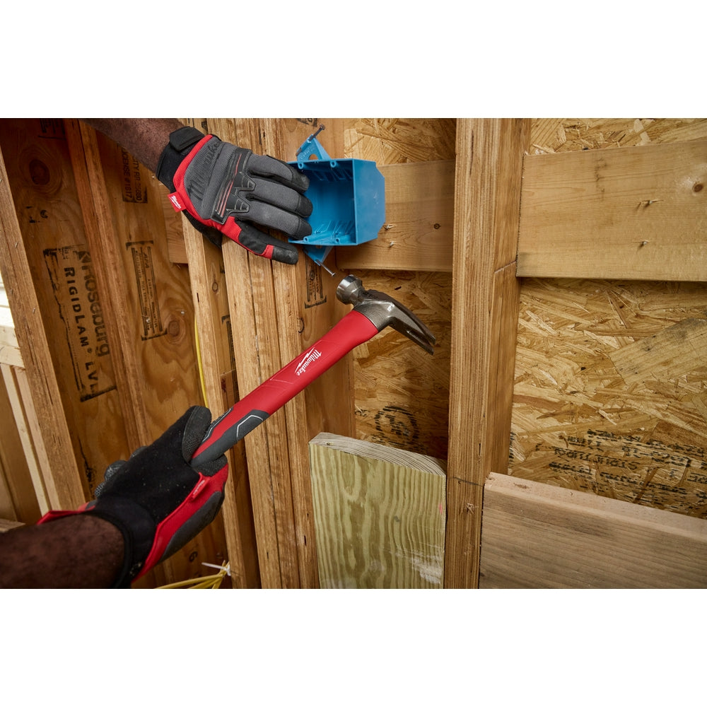 Claw hammer with red fiberglass handle and milled metal head held in gloved hand above wooden surface.