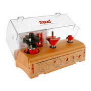 Five router bits with red bases and black cutting surfaces mounted on wooden base in clear plastic case.