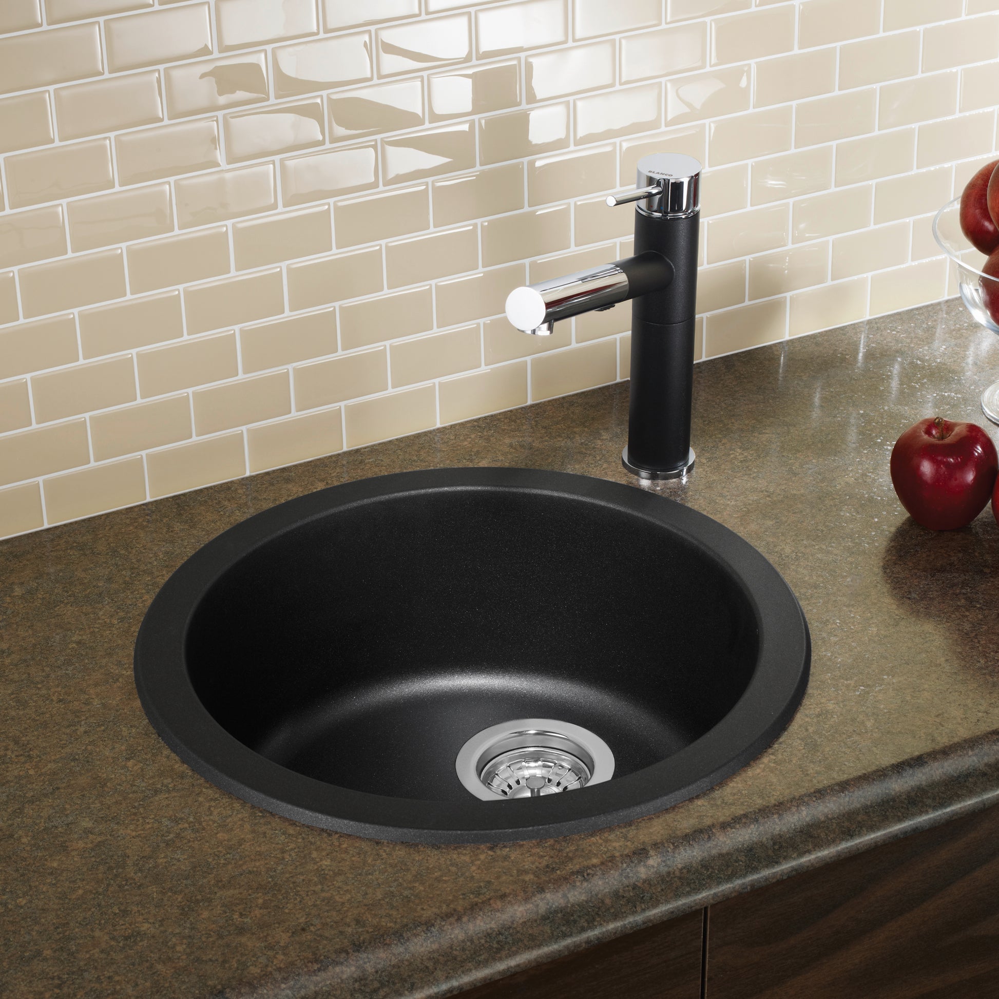 Round anthracite bar sink mounted in countertop with black faucet and white tile backsplash.