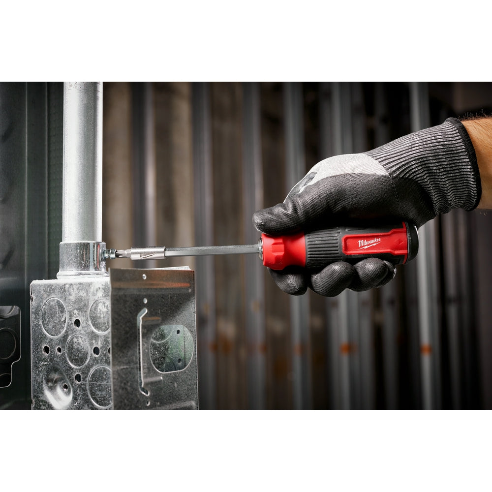 Red and black multi-bit screwdriver held in gloved hand driving screw into metal electrical box.