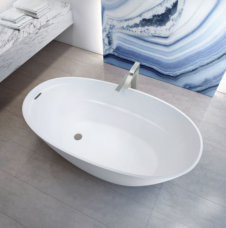 White oval freestanding soaker bathtub with deck-mounted filler in modern bathroom setting.