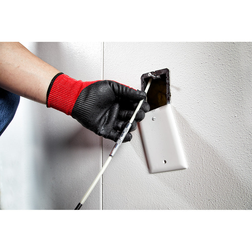 Gloved hand holding a flexible white fish stick tool inserted into an electrical outlet opening in a white wall.
