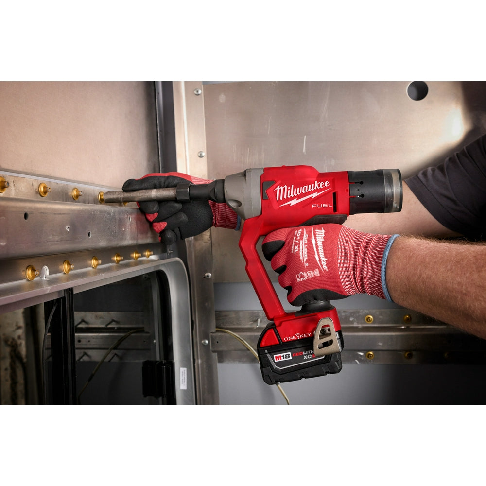 Milwaukee M18 FUEL rivet tool in use on metal surface with operator wearing red work gloves.