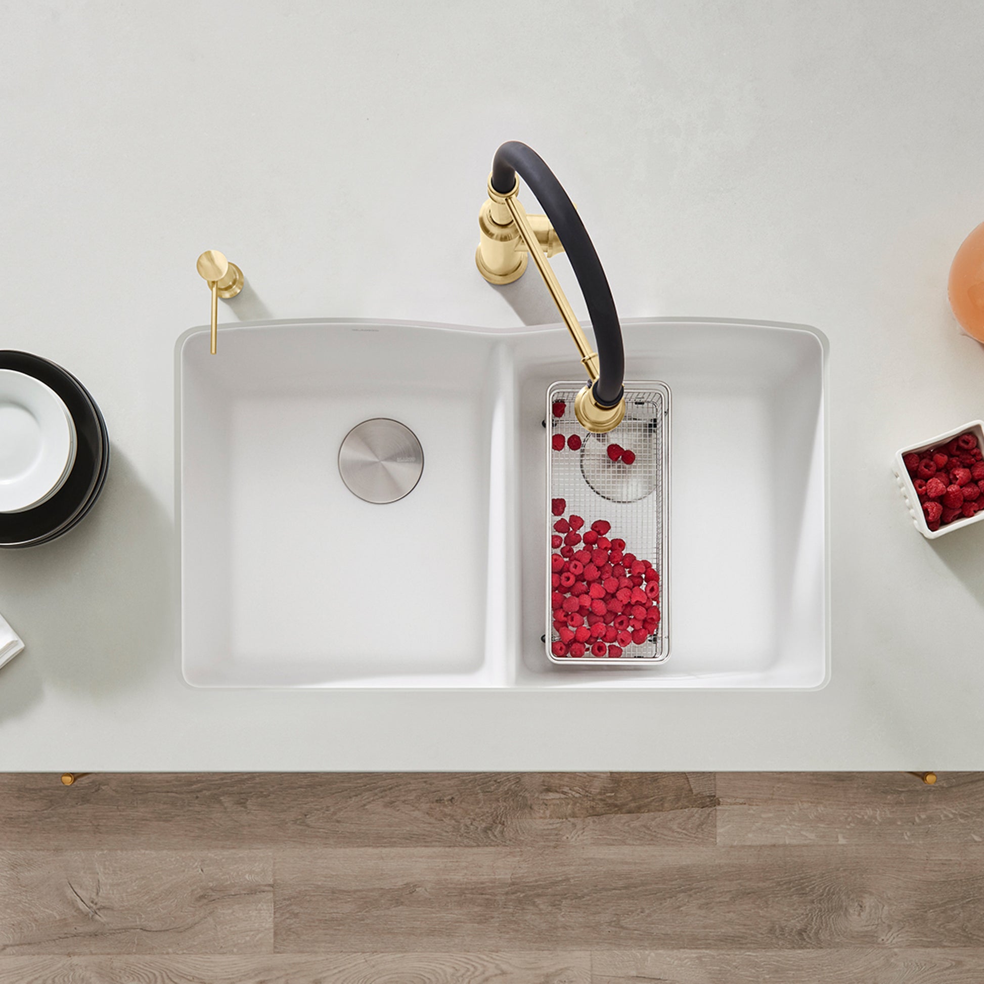 White double bowl undermount kitchen sink with black and brass faucet, viewed from above.