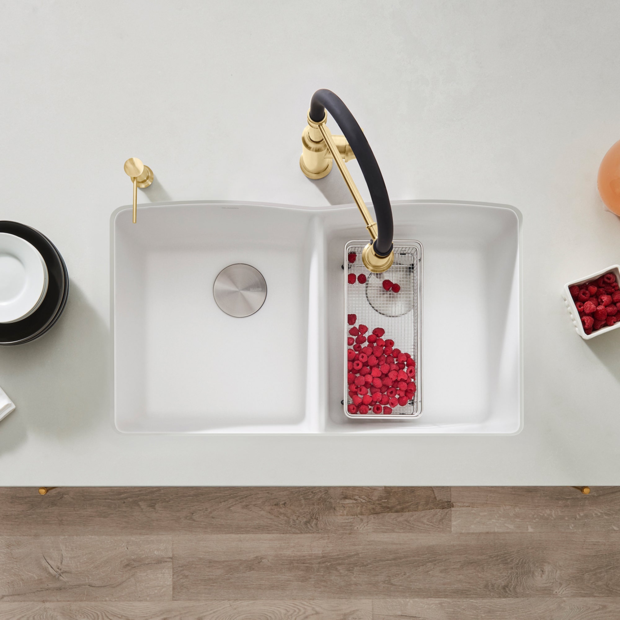 White double bowl undermount kitchen sink with black and brass faucet, viewed from above.
