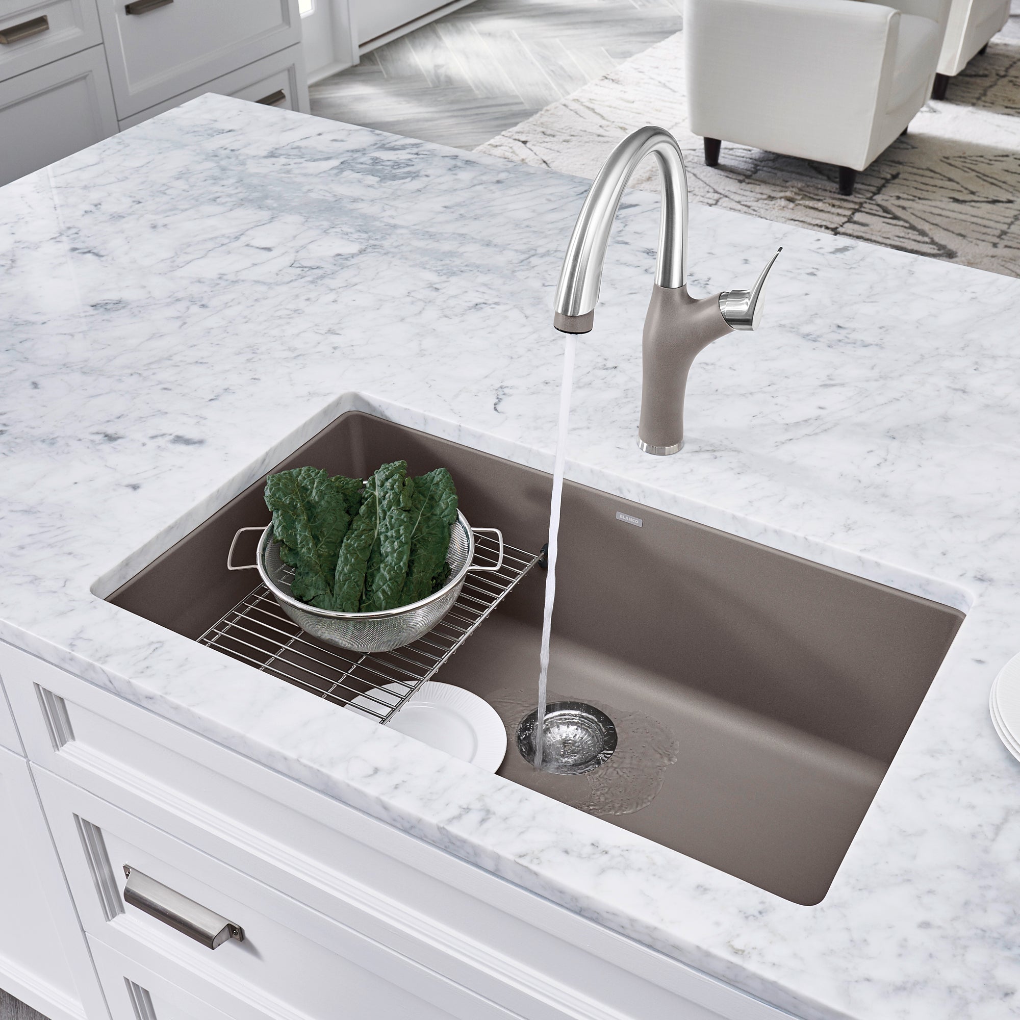 Truffle-colored undermount kitchen sink with single bowl, stainless steel faucet, and grid accessory installed in marble coun
