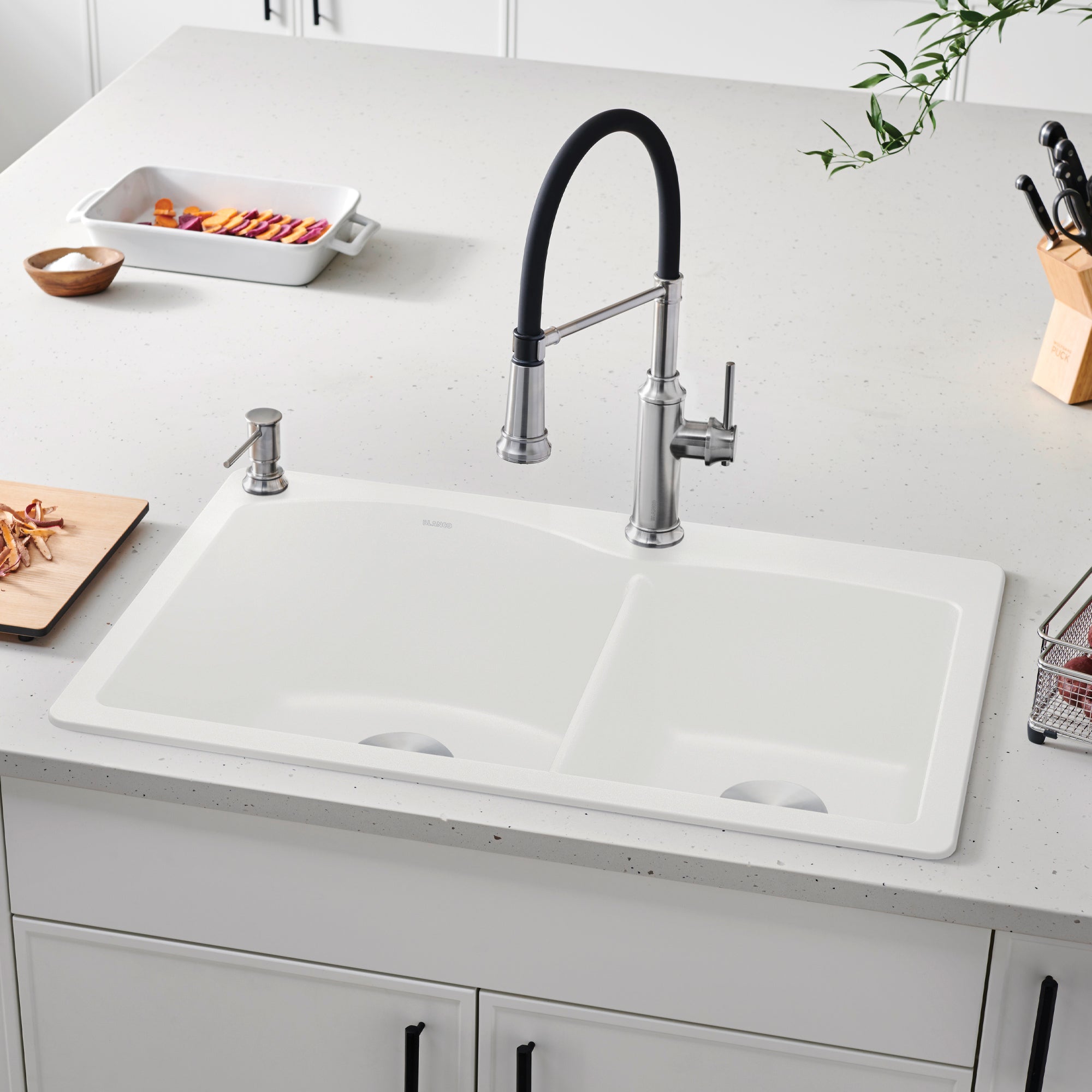 White drop-in kitchen sink with two bowls installed in countertop, paired with pull-down faucet and soap dispenser.