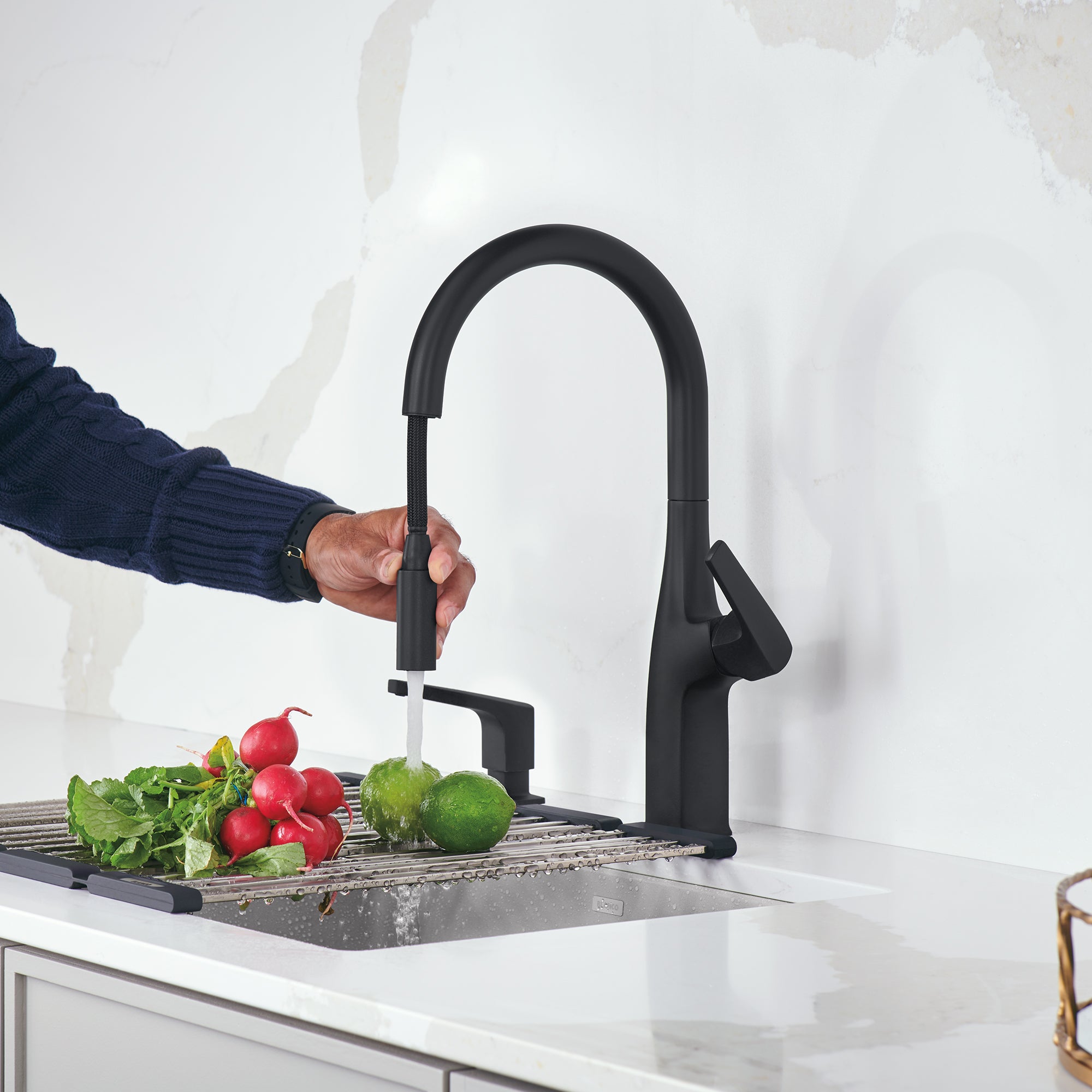 Matte black pull-down kitchen faucet with curved spout and handle, installed over sink with produce below.