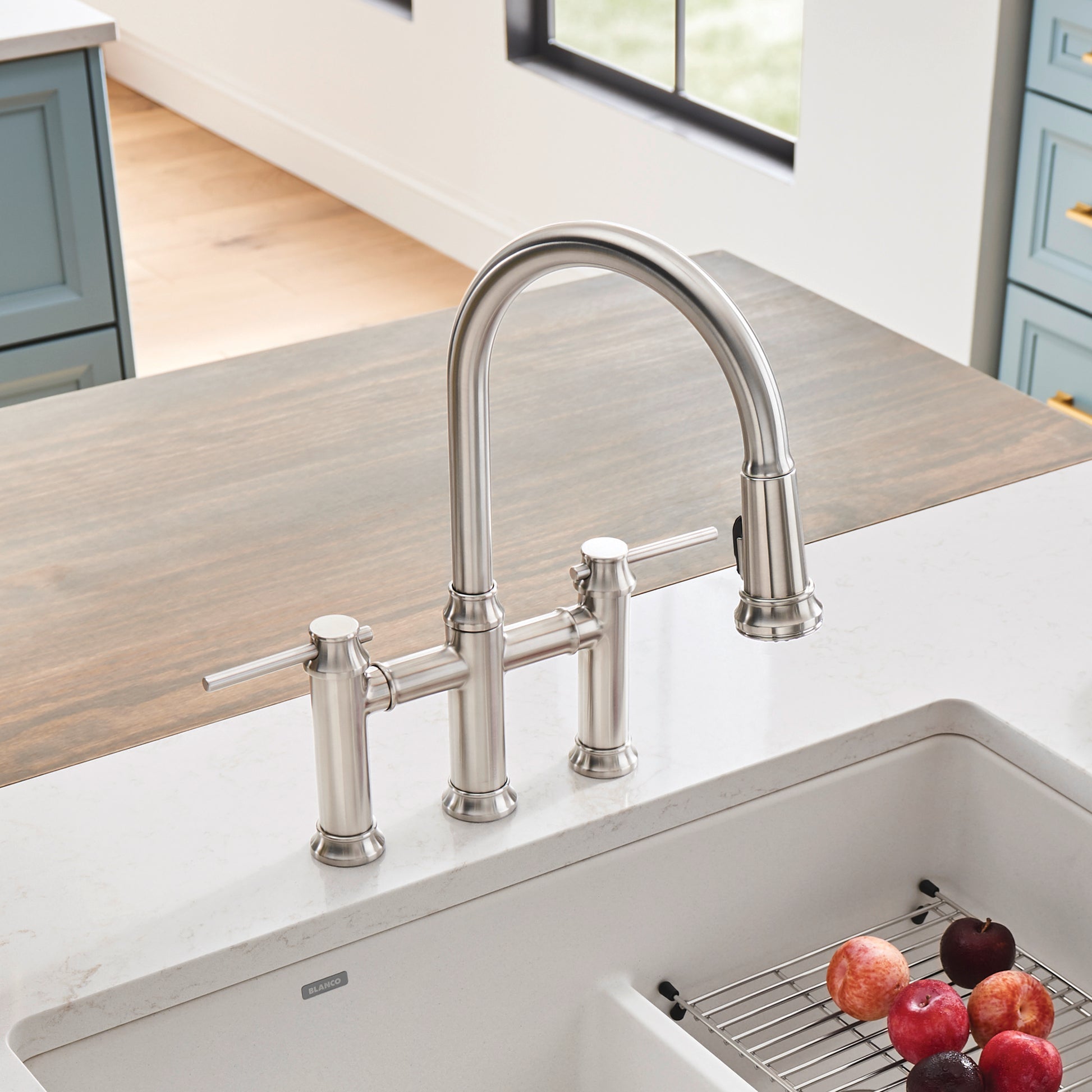 Stainless steel bridge faucet with pull-down spray head and dual handles mounted on kitchen sink countertop.