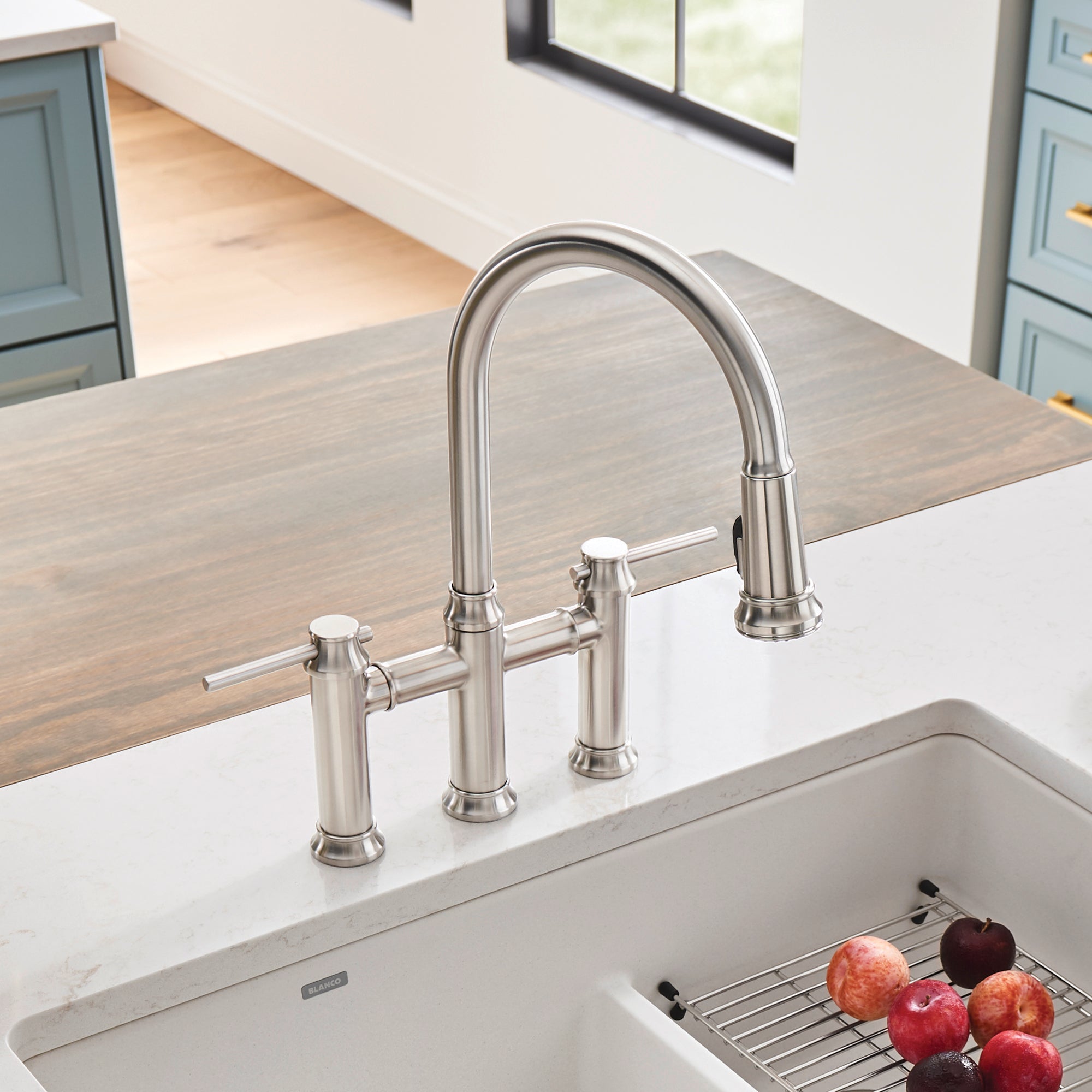 Stainless steel bridge faucet with pull-down spray head and dual handles mounted on kitchen sink countertop.