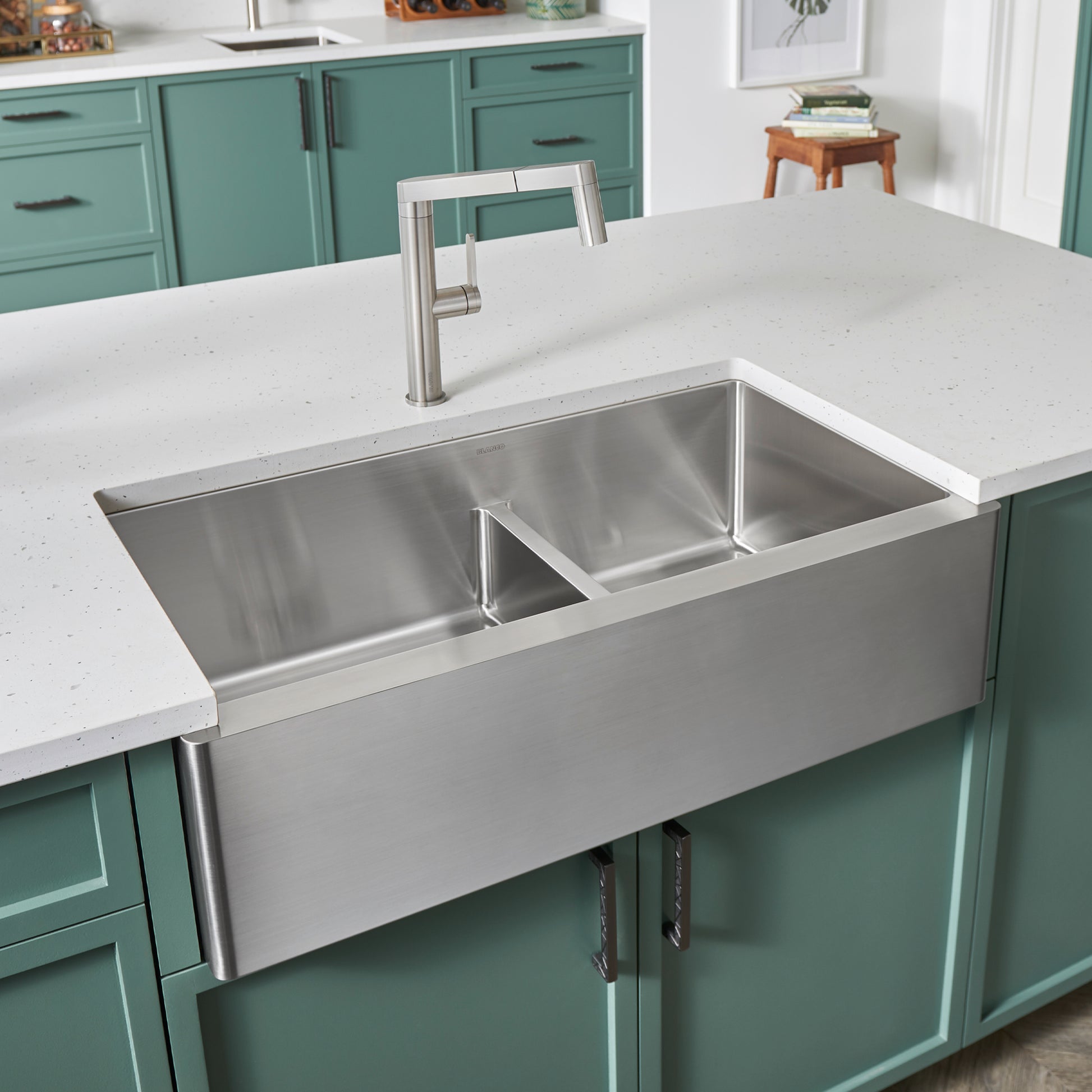 Stainless steel apron front sink with two unequal basins and low divider, installed in white countertop with brushed nickel f