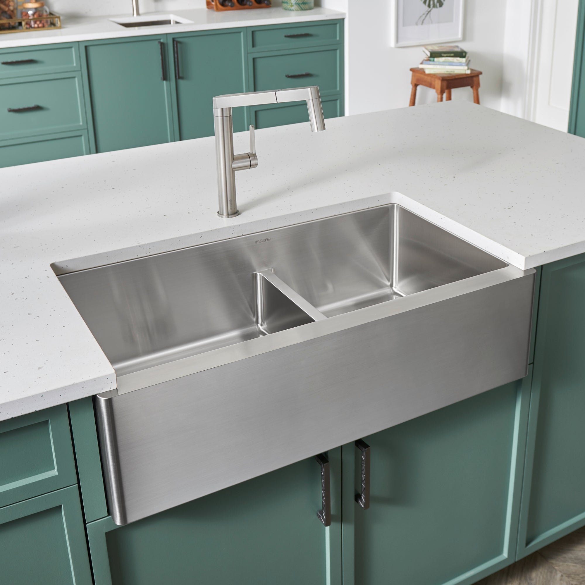 Stainless steel apron front sink with two unequal basins and low divider, installed in white countertop with brushed nickel f