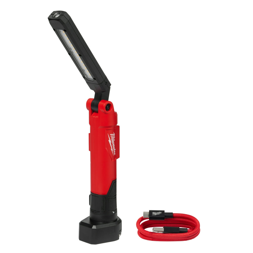 Red and black Milwaukee stick light with LED panel and swivel head, shown with red USB charging cable and black base stand.