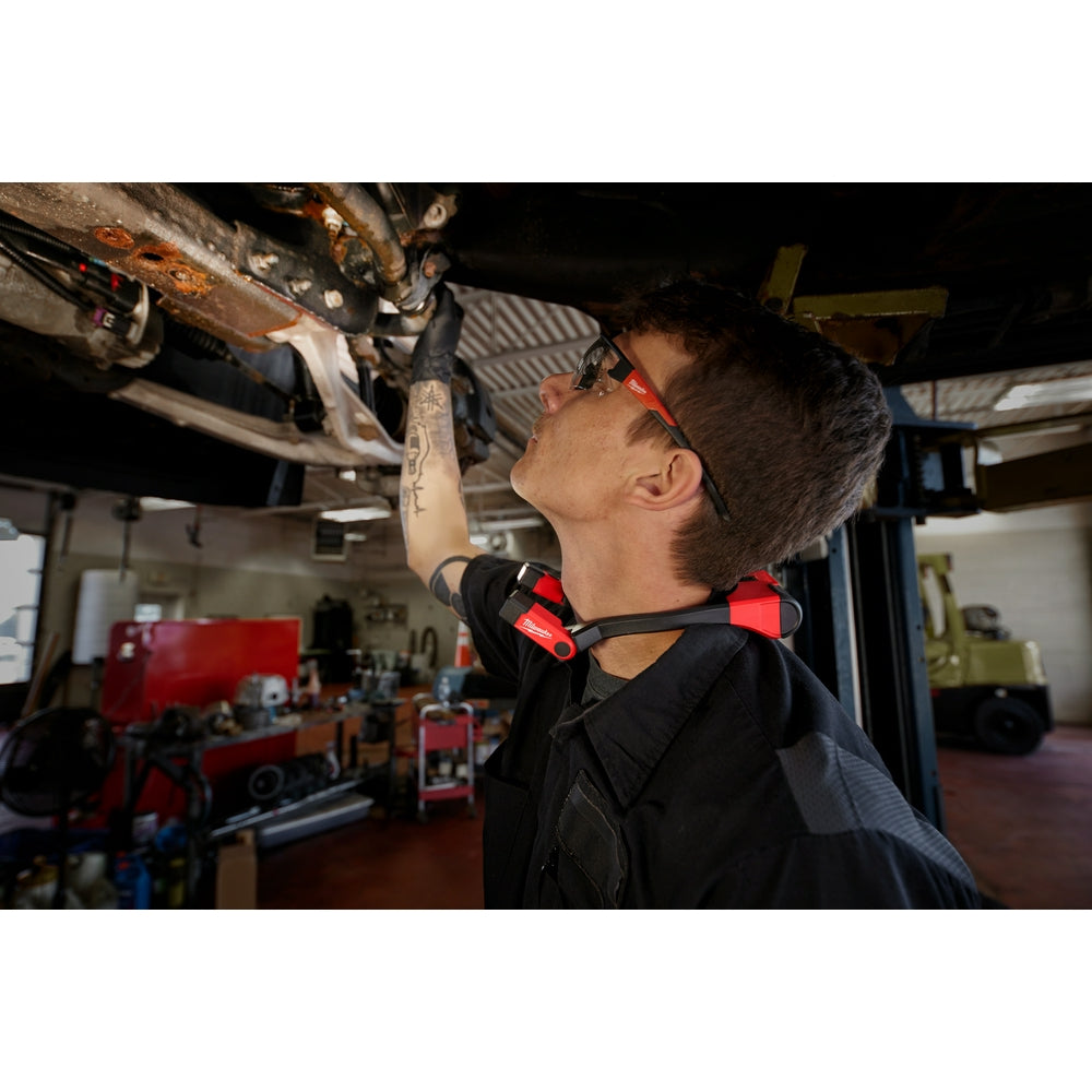 Technician wearing red and black neck light while working overhead on machinery in a garage.