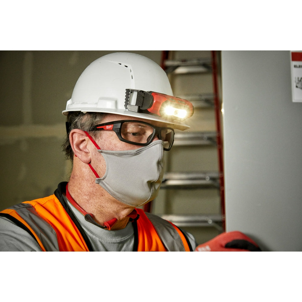 Clear safety glasses with black frames and red temple arms worn by worker in hard hat.