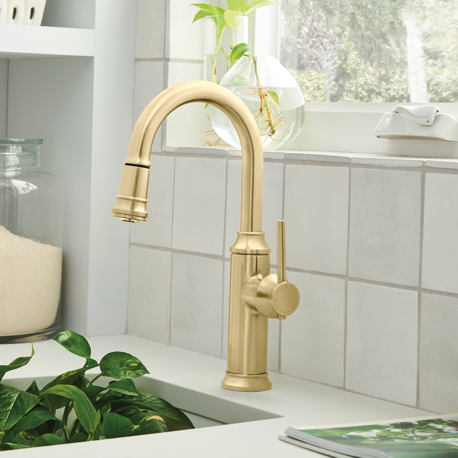 Satin gold pull-down bar faucet with curved spout and round handle mounted on white sink counter.