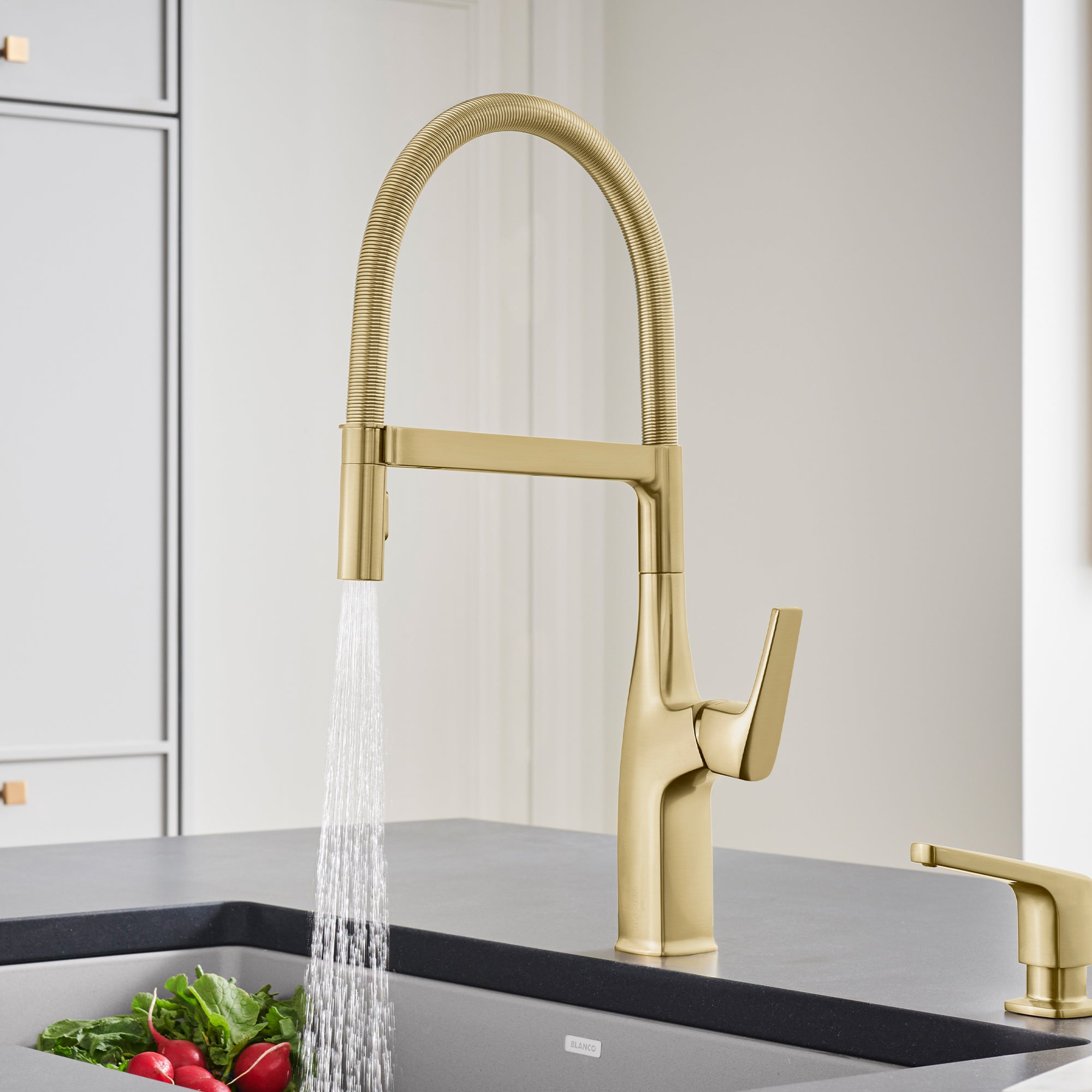 Satin gold semi-pro kitchen faucet with tall curved spout and single lever handle shown installed above sink with water runni