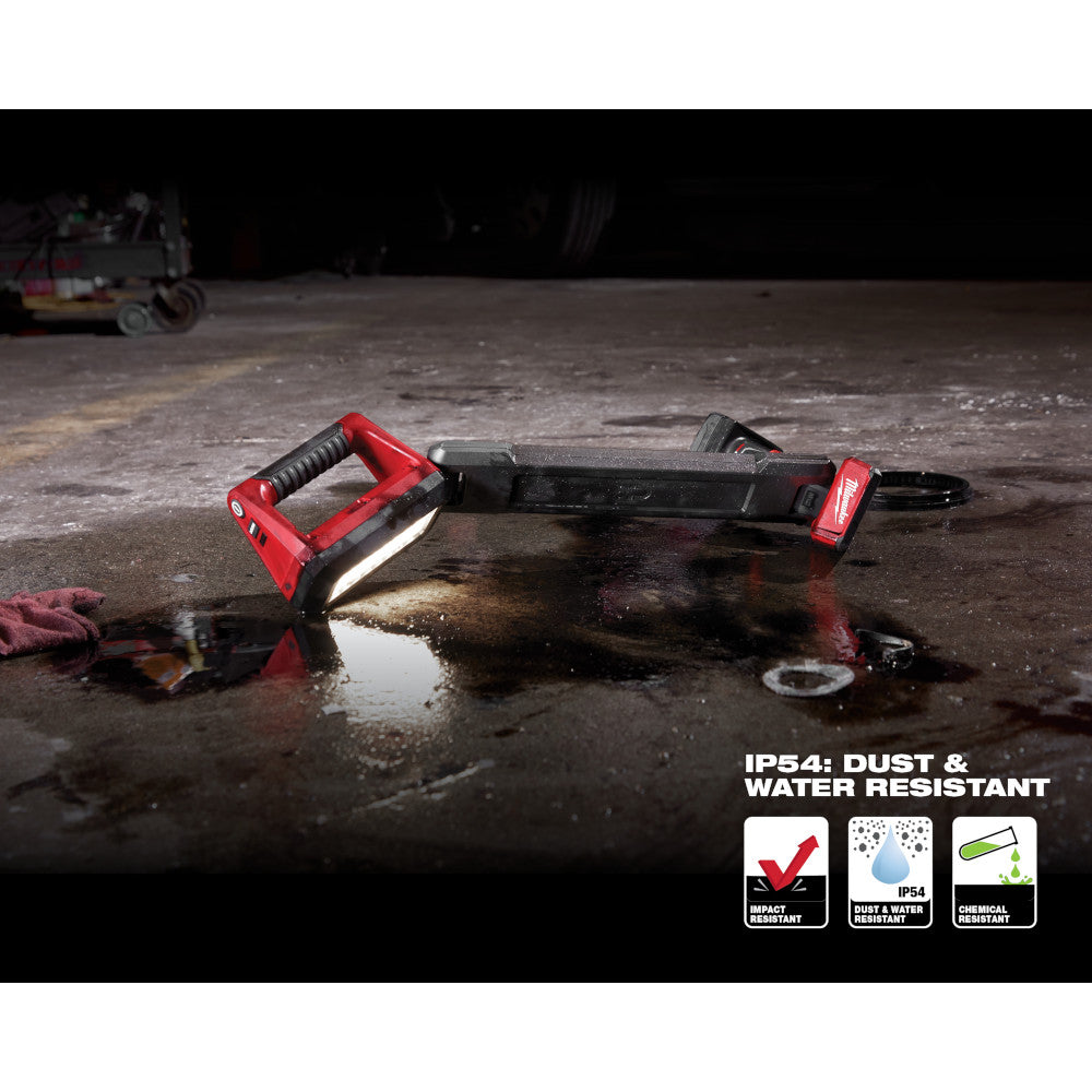 Red and black Milwaukee M12 underbody light with handle, illuminating wet pavement in dark conditions.