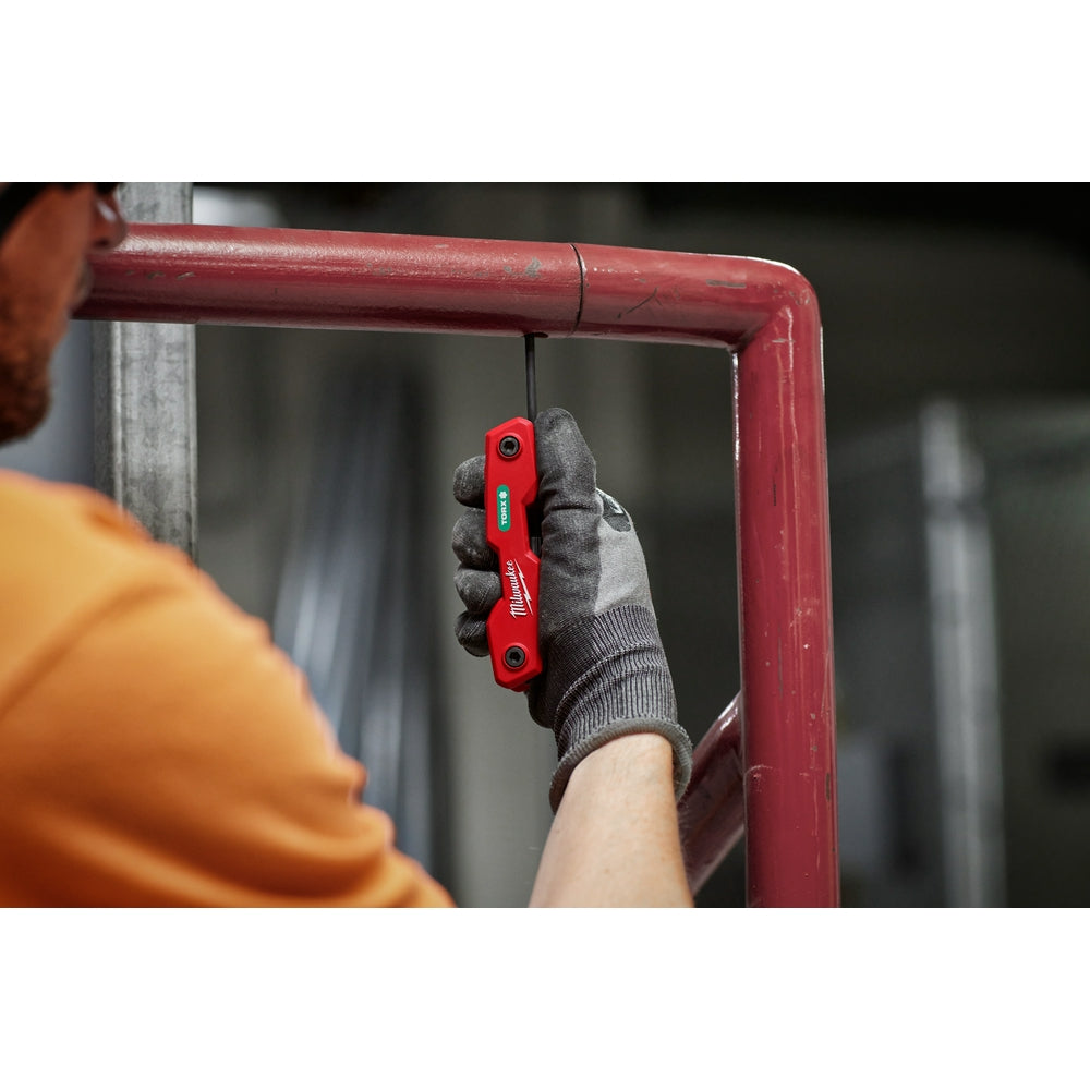 Red folding hex key set with eight Torx keys held in a gloved hand against a red metal frame.