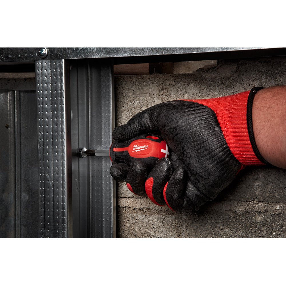 Hand in black and red glove holding red and black Milwaukee screwdriver against metal surface.