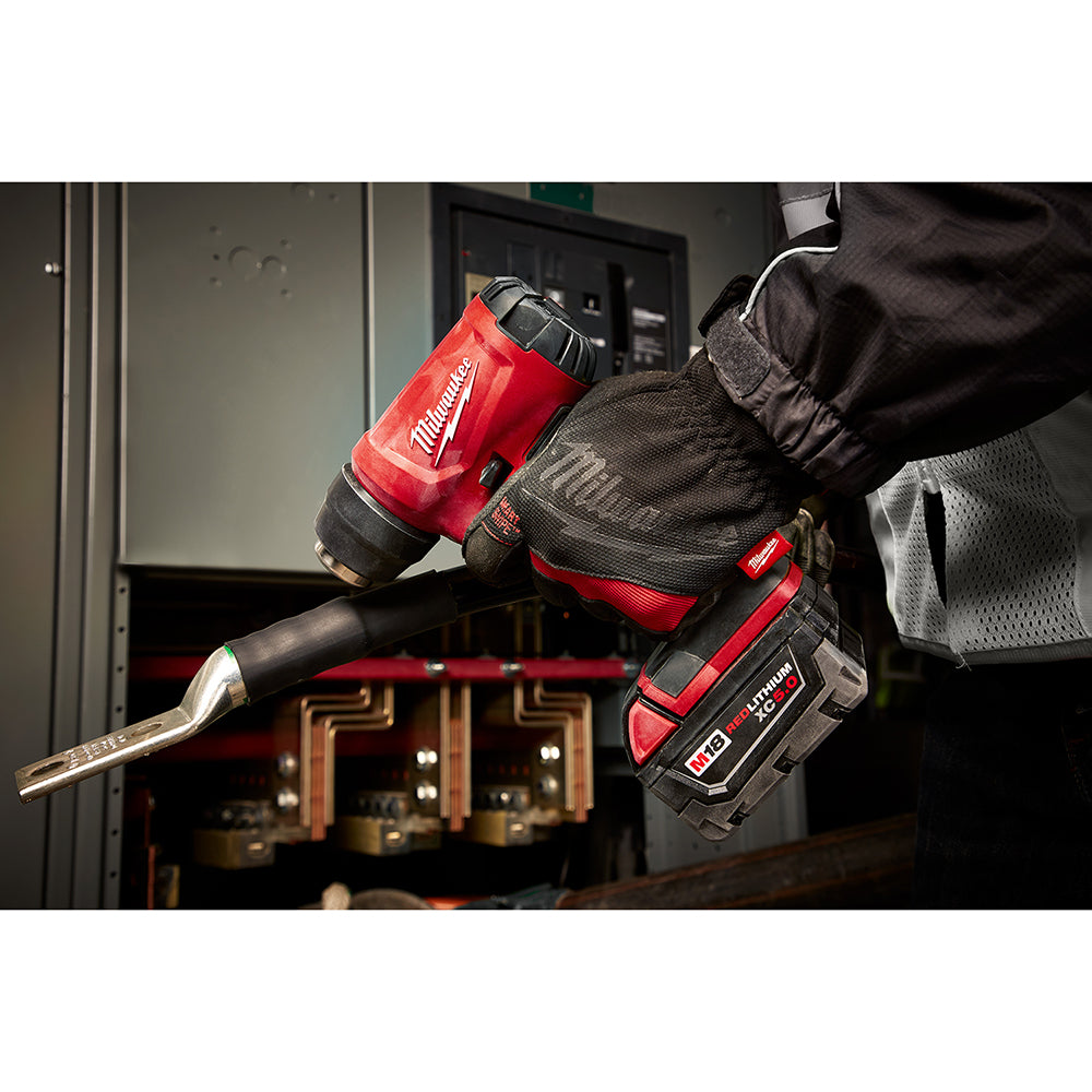 Red and black Milwaukee M18 compact heat gun held in gloved hands with nozzle attachment visible.