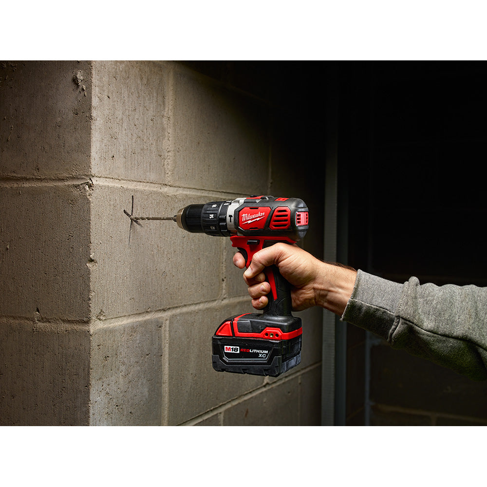 Red and black Milwaukee M18 compact hammer drill/driver with battery being held against a concrete wall.