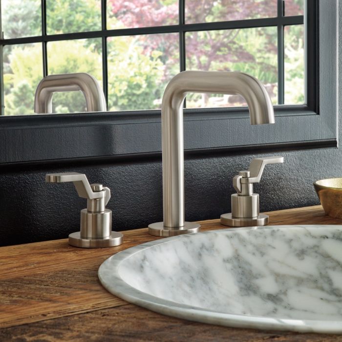 Luxe nickel widespread lavatory faucet with two curved spouts and side handles mounted on marble sink.