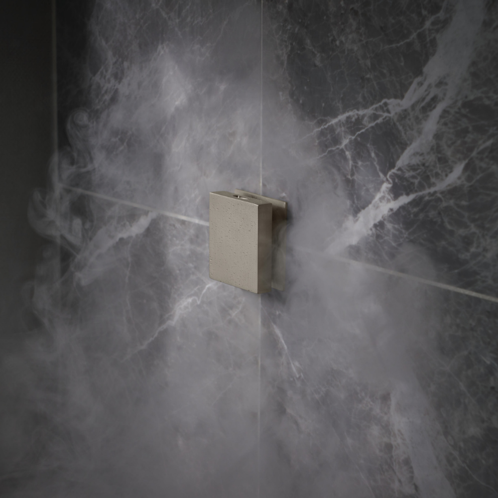Square nickel steam shower control mounted on marble tile wall with water spray.