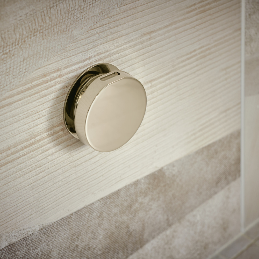 Polished nickel round steam shower control mounted on textured tile wall.