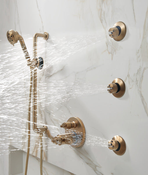 Luxe gold thermostatic valve with six-function diverter and handheld showerhead installed on marble shower wall with water fl